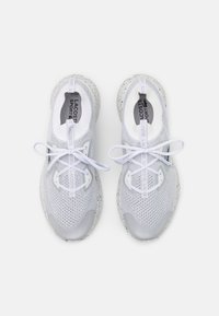 Chaussures de sport blanches à tige en mesh, accents gris texturés et semelles en caoutchouc. Dotées de lacets plats blancs et d'onglets de tirage marqués sur les talons.