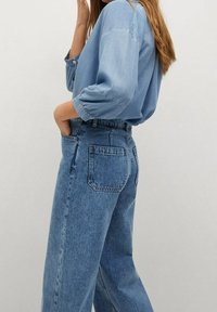 Chemise en denim bleu clair avec manches larges associée à un jean bleu taille haute. Le jean possède une poche arrière et une coupe décontractée.