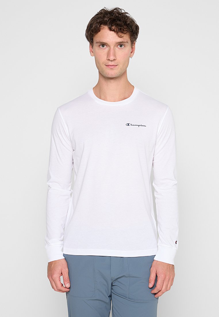 Camiseta blanca de manga larga hecha de suave algodón, con un escote redondo y un pequeño logotipo negro de Champion en el lado izquierdo del pecho.