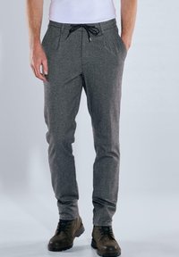 Graue, melierte Jogginghosen mit Kordelzugbund, seitlichen Taschen und schmalem Schnitt, kombiniert mit braunen Schnürstiefeln.