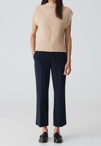 Beige stickad topp med ribbat mönster och flätad design, kombinerad med marinblå vida byxor och bruna loafers. Enkel, modern design.