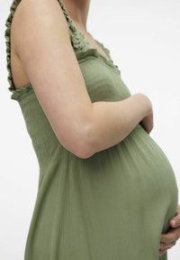 Vestido de maternidad en suave tejido texturizado de color verde claro; cuenta con tirantes con volantes y un corte relajado que se adapta al vientre.