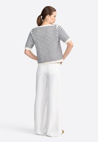 Sweater court en tricot à rayures bleu marine et blanches, avec des manches courtes et un tissu texturé. Associé à un pantalon large blanc.