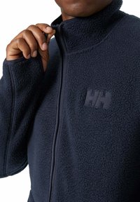 Navy fleece jacket with high collar and zip closure. Features textured fabric, subtle branding, and elasticized cuffs for a snug fit.