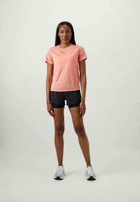 Ανοιχτό ροζ αθλητικό t-shirt με κοντά μανίκια συνδυασμένο με σκούρα σορτς. Μοντέλο που φοράει άσπρα και γκρίζα αθλητικά παπούτσια. Λείος ιστός υφάσματος.