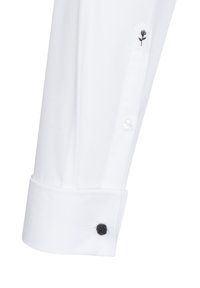 Poignet de chemise blanche avec un bouton de manchette noir noué et une petite broderie de rose noire près des boutons.