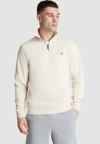 Cream-colored sweatshirt with a quarter-zip, ribbed cuffs, and a penguin logo on the chest. Made from soft, textured fabric.