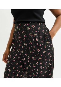 Svarta tygbyxor med ett blommönster som har rosa rosor och små vita blommor. Inkluderar sidfickor och en mjuk textur.