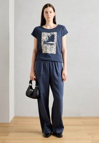 Navy blue cotton t-shirt with a cream graphic design, paired with loose-fitting navy blue linen trousers and a small black handbag.
