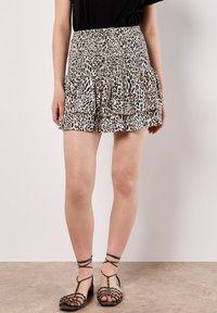 Falda corta de múltiples capas con estampado de leopardo, con cintura fruncida, en tonos beige y marrón. Lleva sandalias planas de tira.