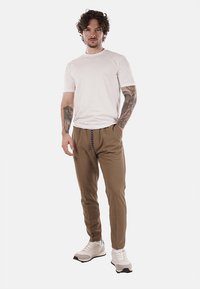Pantaloni beige leggeri con vita elastica e cordino. Abbinati a una camicia bianca aderente e scarpe da ginnastica grigie con accenti neri.