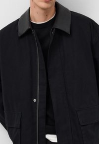 Czarna kurtka z szarym, stojącym kołnierzem; posiada zamek błyskawiczny, dwie przednie kieszenie oraz teksturowaną tkaninę.