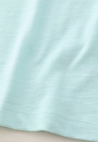 Helle mintgrüne Baumwollstoffe mit einer weichen Textur, die dezente horizontale Linien und eine gesäumte Kante aufweist.