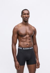 Crne bokserice od glatkog materijala, s bijelim elastičnim pojasom na kojem je ispisano "BJÖRN BORG". Jednostavan i prilagođen dizajn.