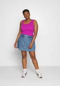 Top sem mangas roxo, saia de denim com fecho de botões à frente e dois bolsos, combinada com ténis brancos com detalhes pretos e design multicolorido.