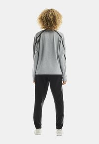 Person with curly hair wearing a gray long-sleeve top with black accents, black pants, and white sneakers, standing facing away.