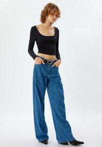 Svart långärmad topp med fyrkantig halsringning, tillsammans med blå vida jeans med diamantmönster och ett svart bälte med silverspänne.