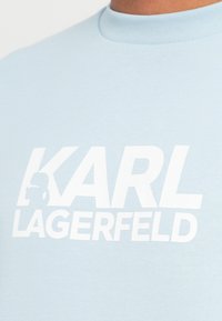 Svetlomodré bavlnené tričko s veľkým bielym logom s textom "KARL LAGERFELD" a grafickým siluetovým prvkom.
