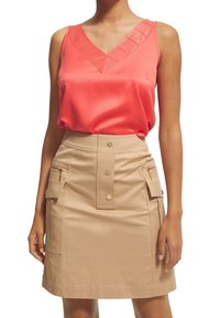 Camisole en satin corail avec décolleté en V, associé à une jupe style utilitaire beige avec des boutons sur le devant et des poches zippées. Texture lisse, design ajusté.