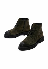 Botines de ante verde oliva con suelas de goma negra, detalles de brogue, cierre de cordones en la parte delantera y cremallera lateral. Diseño de punta redonda.