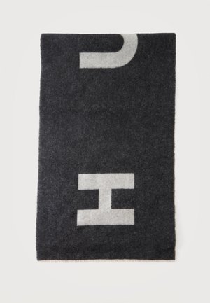 Schwarzer rechteckiger Wollschal mit großen weißen Buchstaben "C" und "H", teilweise sichtbar auf weißem Hintergrund.