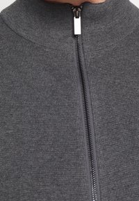 Dark gray zip-up sweater featuring a high collar, ribbed texture, and a contrasting black zipper running down the front.