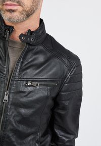 Schwarze Lederjacke mit einem Reißverschluss-Front, Stehkragen, gesteppten Schulterdetails und einer Reißverschlusstasche auf der Brust.
