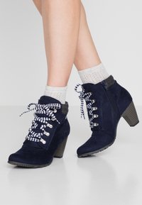 Marineblauwe suède enkellaarsjes met een stevige hak, grijze manchet, gestreepte veters en metalen oogjes. Dikke zool met een gestructureerde afwerking.