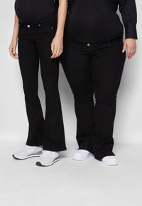Jeans negros com corte flare e perna reta, com bolsos frontais. Um par é combinado com ténis brancos, e o outro com sapatilhas de desporto cinza claro.
