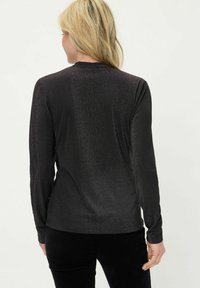 Zwarte top met lange mouwen en een glanzende, gestructureerde afwerking. Voorzien van een ronde halslijn en een aansluitende pasvorm, met lange mouwen en een subtiele glans.