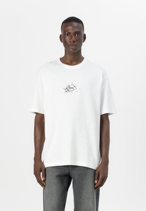 T-shirt oversized blanc avec un imprimé effet craquelé portant "BOSS" au centre. Fabriqué en coton, avec des manches courtes et un col rond.
