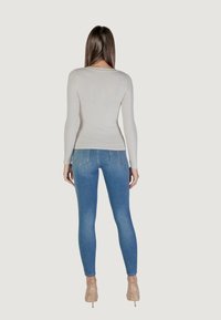 Maglietta attillata beige a maniche lunghe abbinata a jeans skinny blu chiaro, che mostrano una texture liscia e dettagli di cucitura in denim standard.