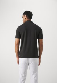 Polo preta de manga curta com gola clássica, design ajustado e textura suave, combinada com calças brancas.