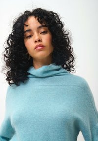 Helles blaues Strickpullover mit Kragen, der eine weiche Textur und eine lockere Passform aufweist. Zu den Details gehören gerippte Ärmelbündchen und nahtlose Schultern.
