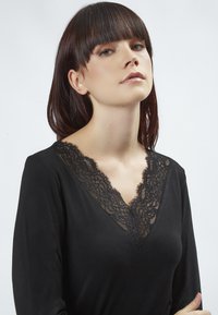 Schwarzes Langarmoberteil mit tiefem V-Ausschnitt und zarten schwarzen Spitzendetails am Ausschnitt, glattes Material mit einem subtilen Glanz.