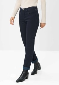 Dunkelblaue Jeans mit schmaler Passform, hohem Bund, Fronttaschen und umgeschlagenen Säumen. Kombiniert mit schwarzen Stiefeletten.