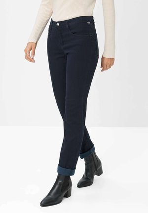 Dunkelblaue Jeans mit schmaler Passform, hohem Bund, Fronttaschen und umgeschlagenen Säumen. Kombiniert mit schwarzen Stiefeletten.
