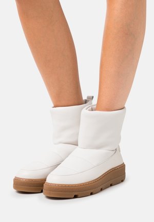 Stivaletti alla caviglia trapuntati bianchi con risvolto, caratterizzati da una suola spessa marrone e sottili dettagli di cuciture. Texture in pelle liscia.