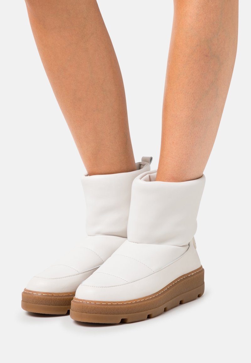 Bottines blanches matelassées avec un revers replié, dotées d'une semelle épaisse marron et de discrètes surpiqûres. Texture en cuir lisse.