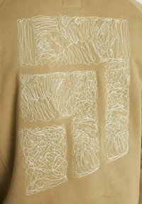 Tessuto beige con design astratti ricamati in bianco e intricate linee, disposti in due forme rettangolari al centro.