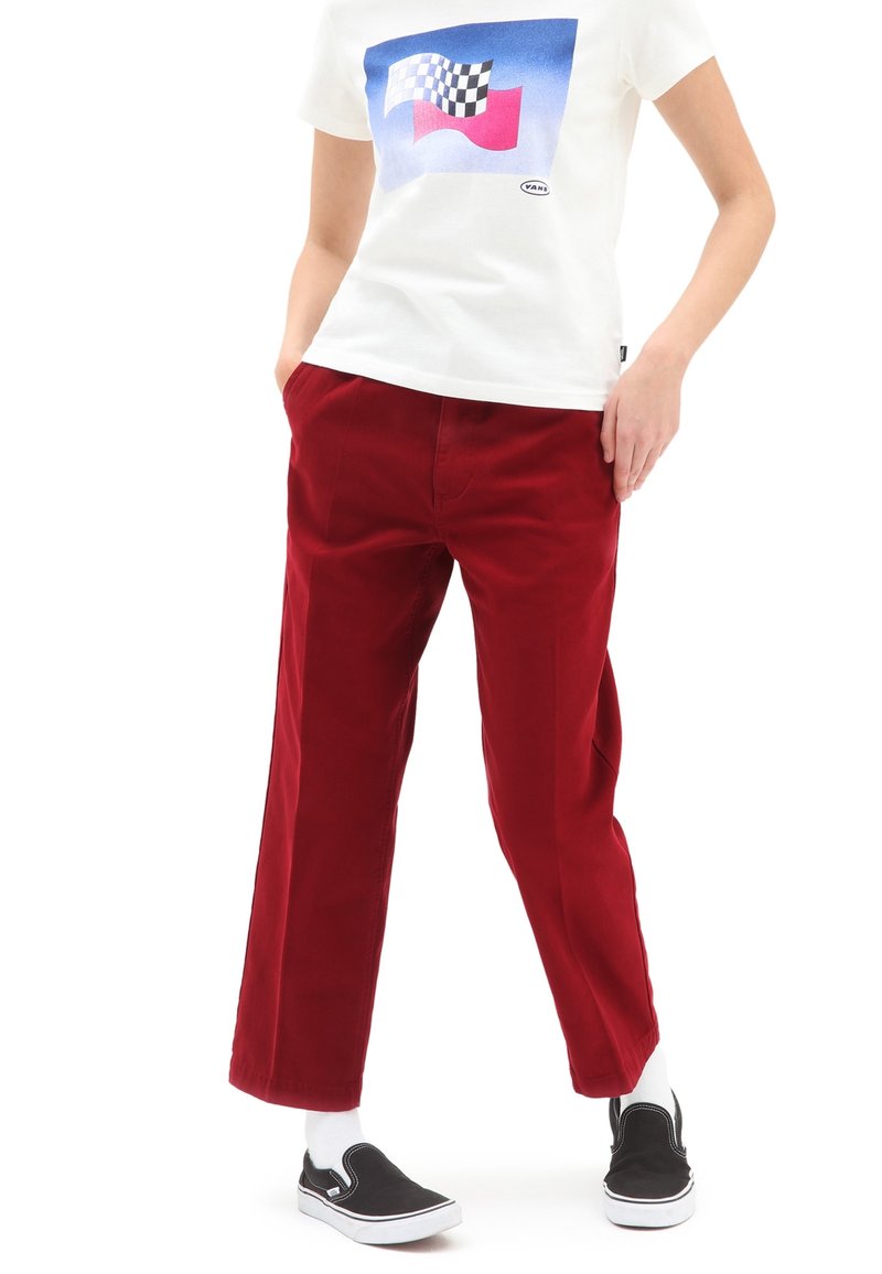 Pantaloni in corduroy rossi con vestibilità rilassata, abbinati a una t-shirt bianca a maniche corte con un design grafico colorato e sneakers nere.