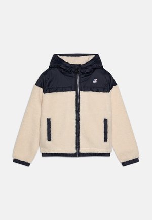 Veste polaire crème avec panneau en nylon noir sur la poitrine, capuche, fermeture éclair devant, poignets élastiques et deux poches latérales.