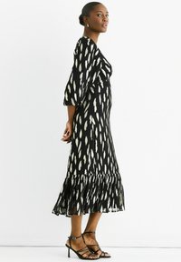 Maxi dress in black with white leaf patterns, featuring balloon sleeves and a ruffled hem. Styled with strappy black sandals.