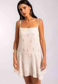 Vestido beige claro con tirantes finos, tela semi-translúcida, dobladillo acampanado y acentos en patrón dorado vertical. Textura suave.