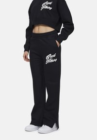 Zwarte cropped sweatshirt met witte tekst "Good for Nothing" op de voorkant, gecombineerd met bijpassende zwarte joggingsbroek met zijzakken en logo-accent.