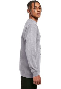 Sivá mikina s dlhými rukávmi, rebrovanými manžetami a okrúhlym výstrihom. Bočný pohľad ukazuje uvoľnený strih a jemnú textúru.