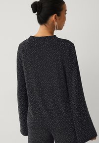 Zwart gestructureerd topje met lange, uitlopende mouwen en een ronde hals, met kleine witte vlekken verspreid over de stof.