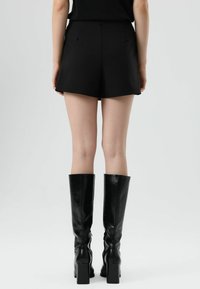 Zwarte korte broek met strakke lijnen en een hoge taille, gecombineerd met kniehoge zwarte leren laarzen met een vierkante hak. Gladde textuur.