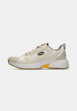 Zapatilla deportiva en crema y gris claro con acentos amarillos y marrones, parte superior texturizada y una suela blanca gruesa con un patrón de dibujo marrón.