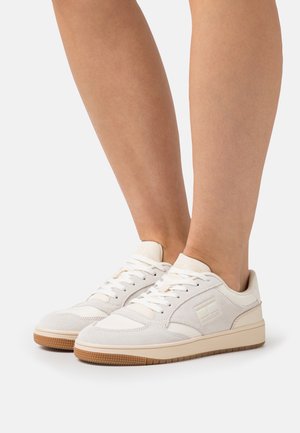 Białe trampki z teksturowanym zamszem i gładkimi skórzanymi akcentami. Posiadają sznurowany wzór, wyściełany kołnierz i gumową podeszwę zewnętrzną.